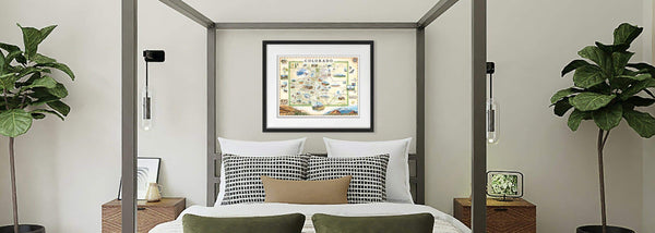 Colorado state map in a black frame hanging above a bed with plants on both sides.
