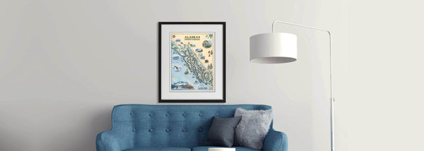 Blue couch with furry pillow and a lamp displaying Alaska’s Inside Passage framed map art by Chris Robitaille.