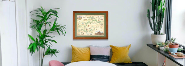 Badlands National Park hand-drawn map in a wood frame hung on a wall above a couch near a cactus. 