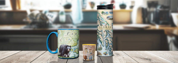 Xplorer Maps drinkware including Travel To Go Mug, Ceramic Mug, and Ceramic Shot Glass sitting on a kitchen butcher block counter. 