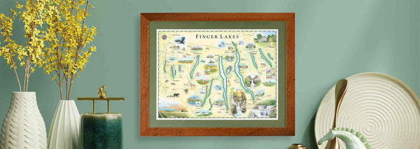 Framed Finger Lakes hand-drawn maps hanging on a green wall. Nest to the art are yellow flowers. 