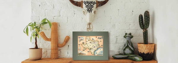 Texas State Mini Map by Xplorer Maps. The pre-matted map is leaning against a brick wall next to cactus and frog. Hanigng above is a cow skull. 