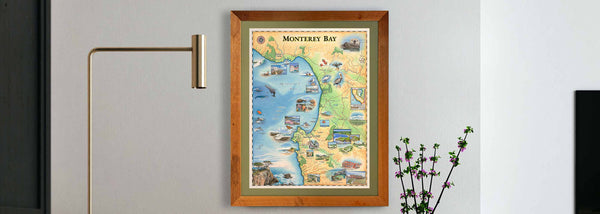 Hand-drawn story map of Monterey Bay, California hanging on a wall. This unique map beautifully encapsulates the bay's allure, presenting its rugged coastline, lively marine life, and iconic landmarks with exceptional artistry.