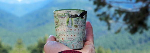 Xplorer Maps Shot glass of Olympic National Park Map being held by a man on a mountain top. 