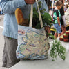 A man shopping at a farmers market with an Alaska Map Tote Bags by Xplorer Maps. The tote bag is filled with bread and vegetables.