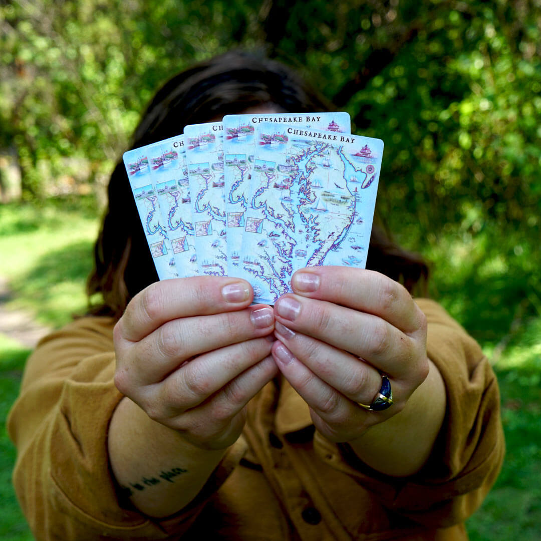 A person holding five Chesapeake Bay playing cards in front of their face. Park Like background.