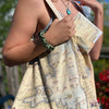 A woman carrying a Flathead Lake Montana Map Canvas Tote Bag featuring Golfing, Rafting, birds, eagles, Osprey, Bears, deer, mountain lion, fish, Cherry Blossoms, and flowers like Glacier Lilies and Lady Slippers.