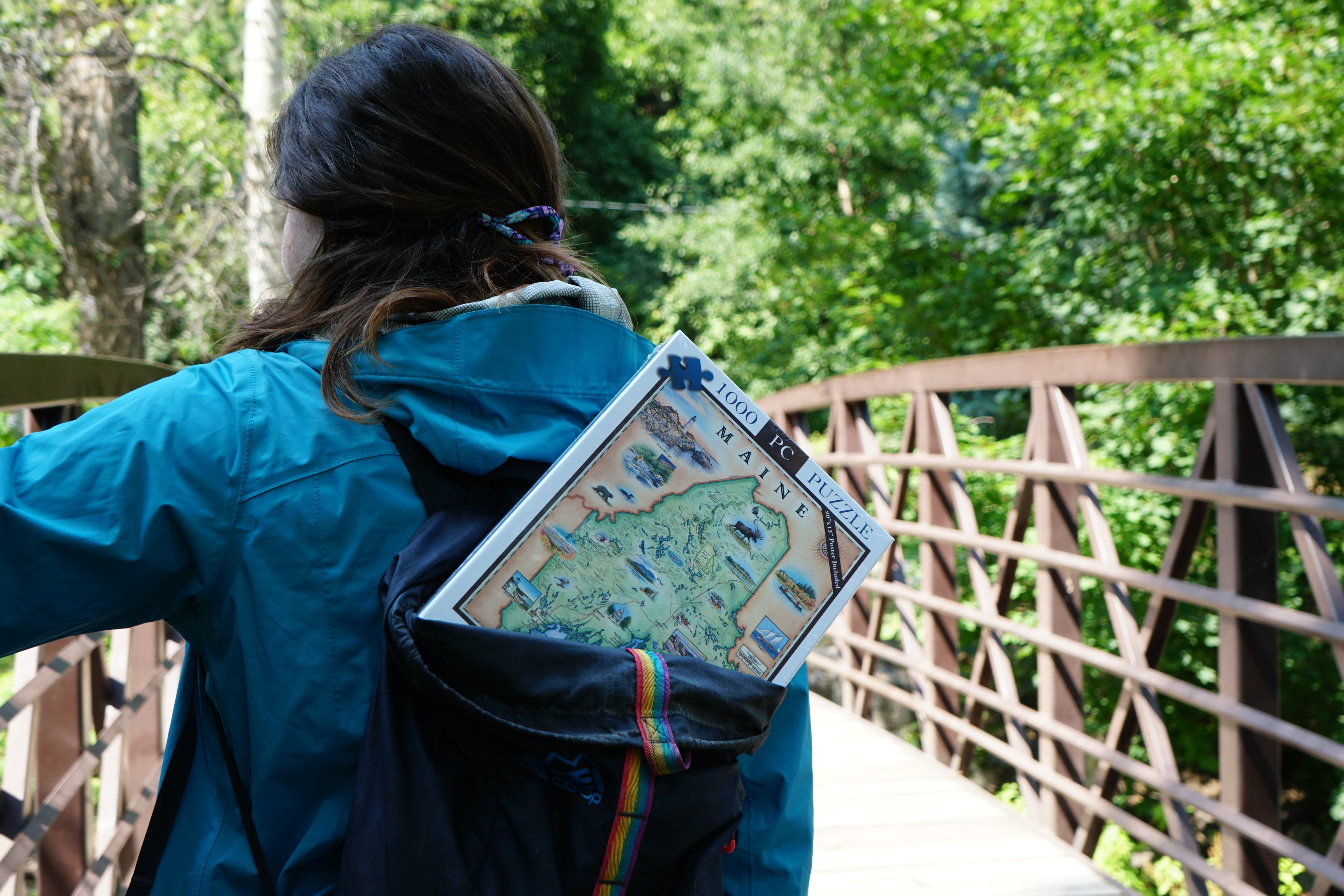 Maine puzzle in a backpack of a women cross a bridge in nature.
