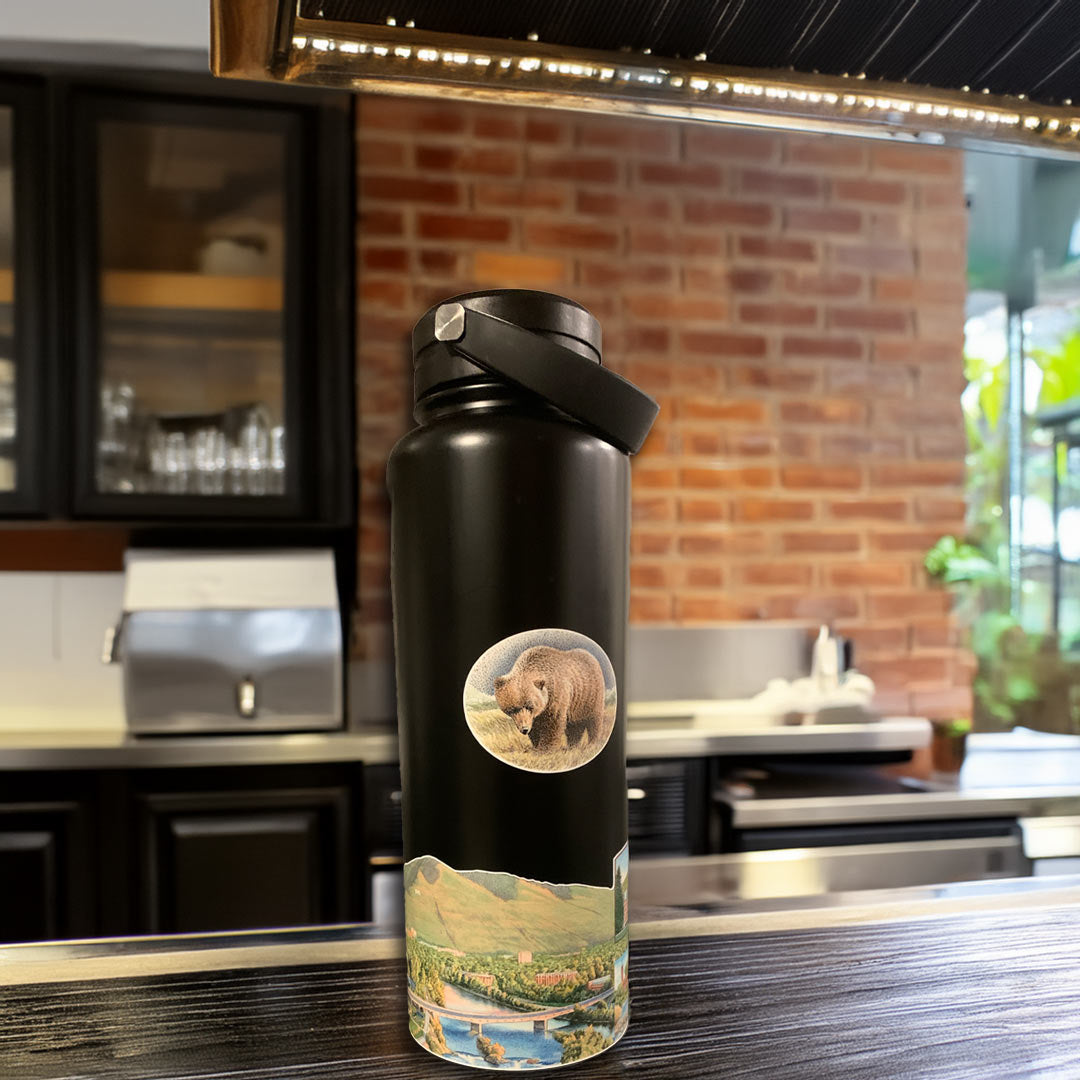 Missoula Map Wrap on a Black Stainless Steel Water Bottle. The bottle is sitting on a dark wood counter with a brick wall in background.