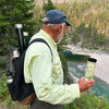Man with a Montana travel Dirnkware looking at a river. The man has a back pack with fly rods in it.