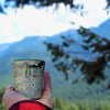 Person holding an Olympic National Park Map ceramic shot glass outside in the mountains.