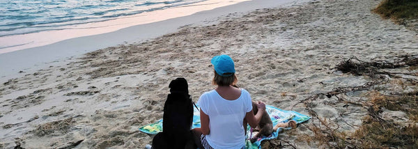 Lady with her black lab sitting on a a beach in Hawaii with an Xplorer Maps Fleece Blanket. 