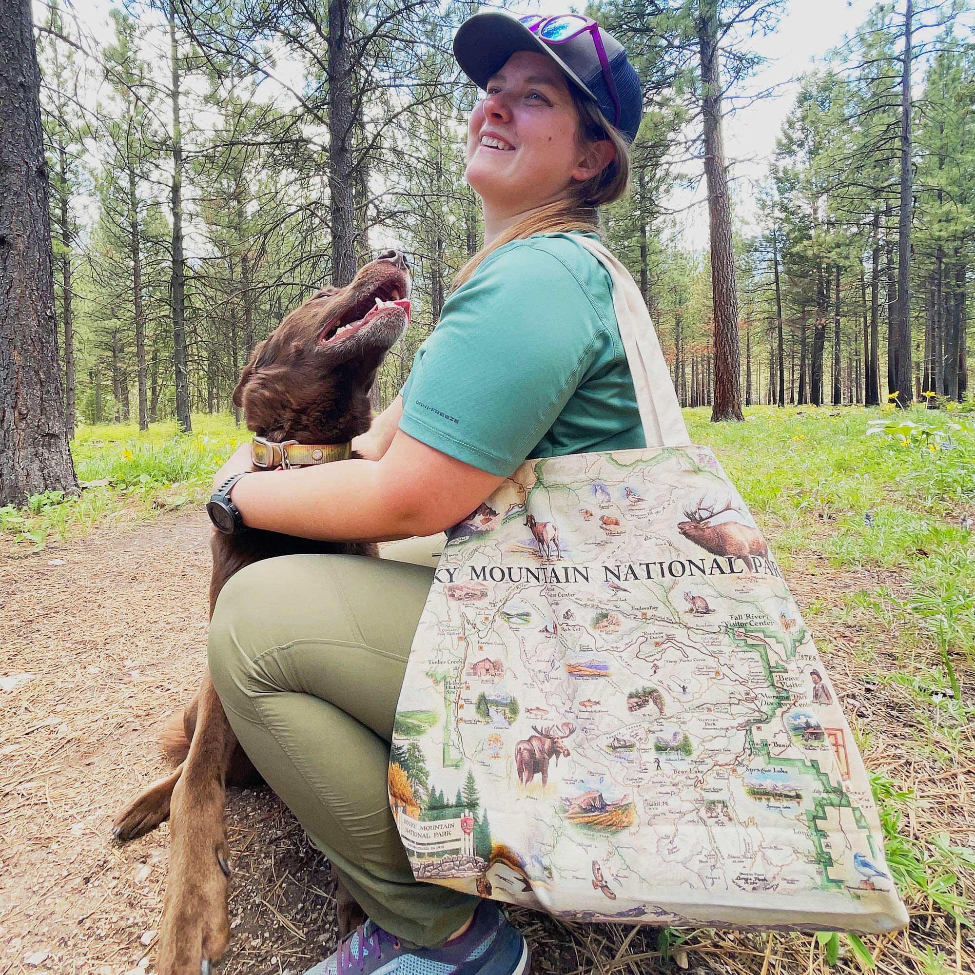 A woman hugging her dog with a Rocky Mountain National Park Map Canvas Tote Bag around her shoulder.