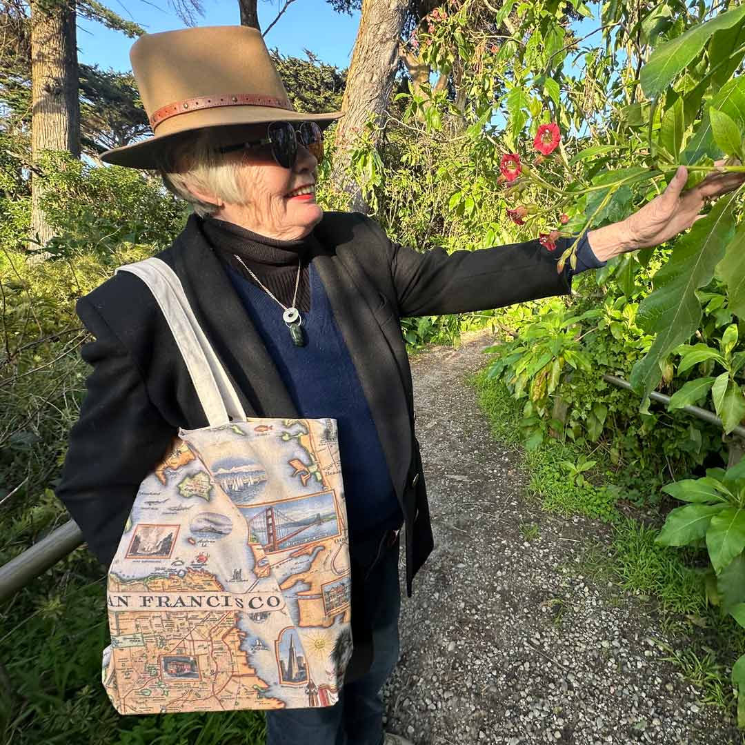 Elder Lady with a San Francisco canvas tote bag holding a flower in a garden.