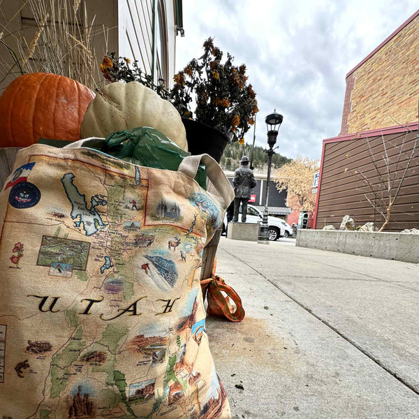 A Utah Canvas tote bag sitting in front of an orange pumpkin and a white pumpkin.