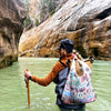 Women walking in a river canyon in Zion with the Zion National Park pouch tote back over her shoulder.