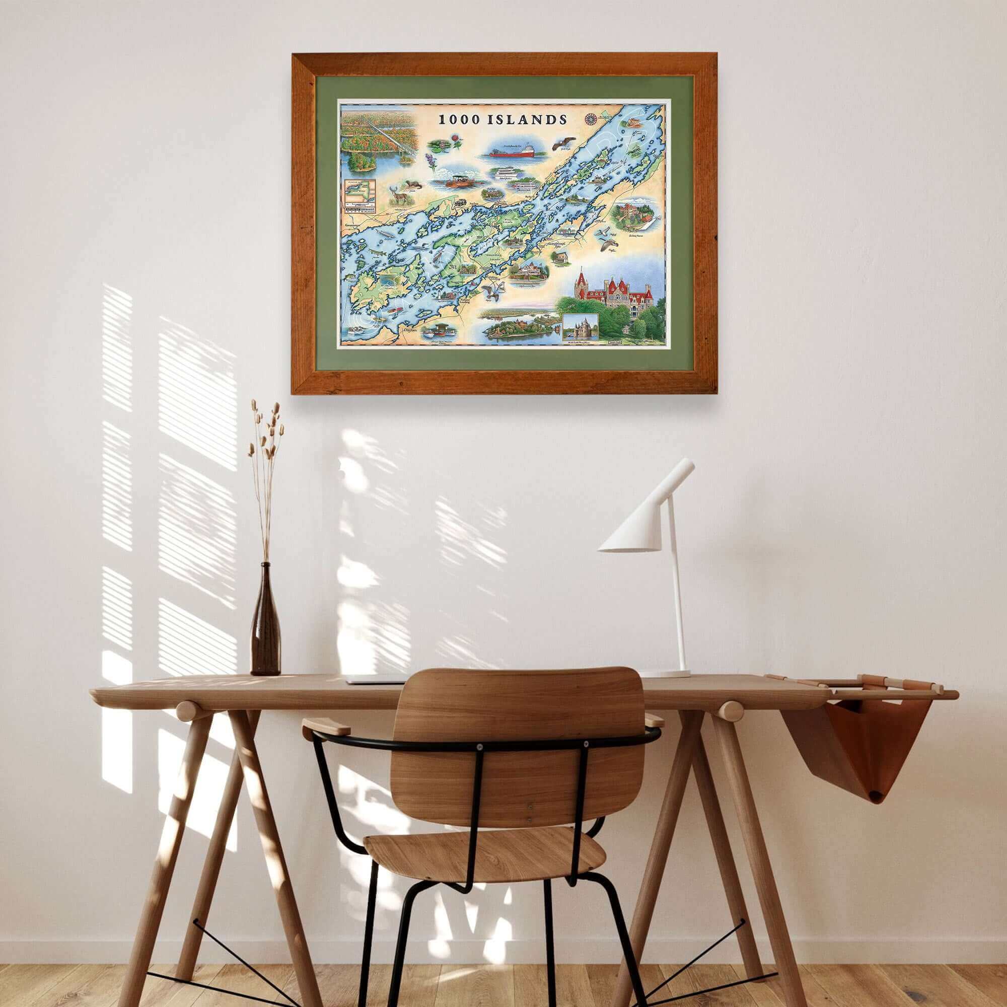 1000 Islands framed hand-drawn map with green mat hanging over a wooden desk and chair.