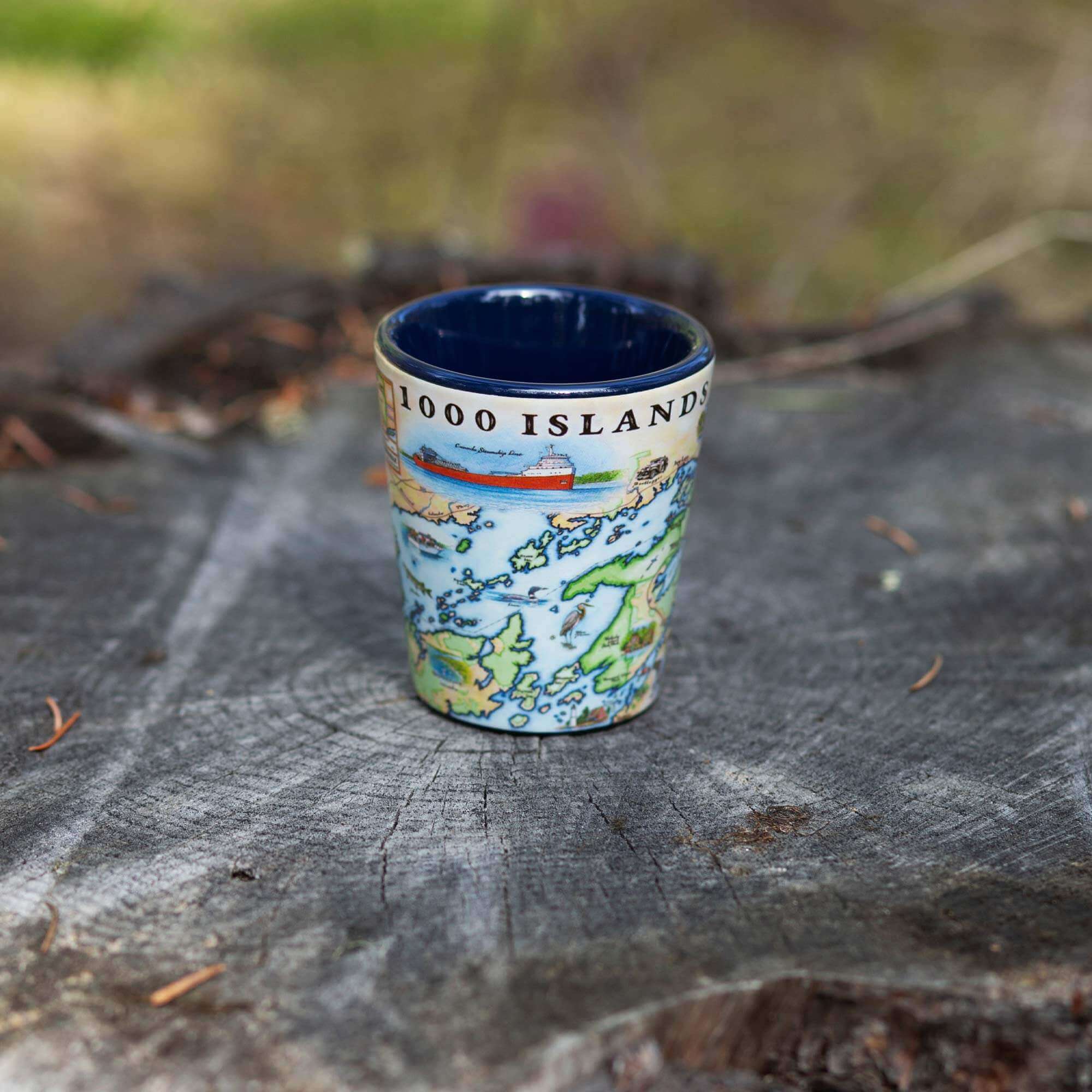 Blue 1000 Island Map Ceramic Shot Glass sitting on a tree stump.