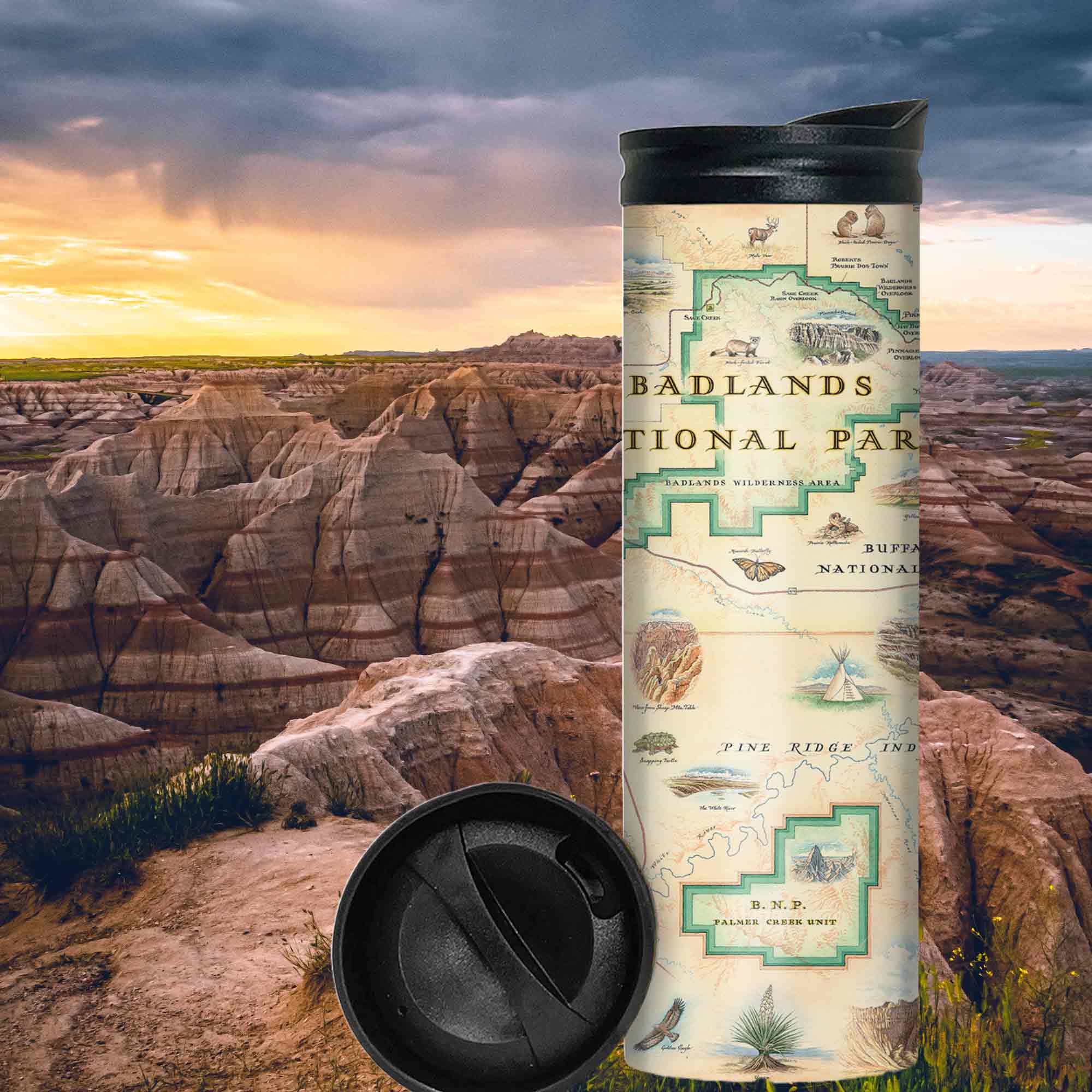 Badlands National Parks Map Travel Drinkware in the mountains during sunset. The backdrop is of Grand Staircase–Escalante National Monument in southern Utah. The map features Buffalo Gap Grasslands, Vulture Peak, and Yellow Mounds Overlook. Flora and fauna of Jasper Tree, Yucca plant, deer, dinosaurs, birds, and fox.
