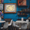 Xplorer Maps' Mallorca Island hand-drawn map hanging on a blue wall in a European restaurant.