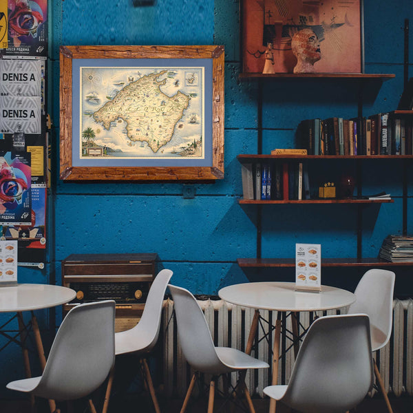 Xplorer Maps' Mallorca Island hand-drawn map hanging on a blue wall in a European restaurant.