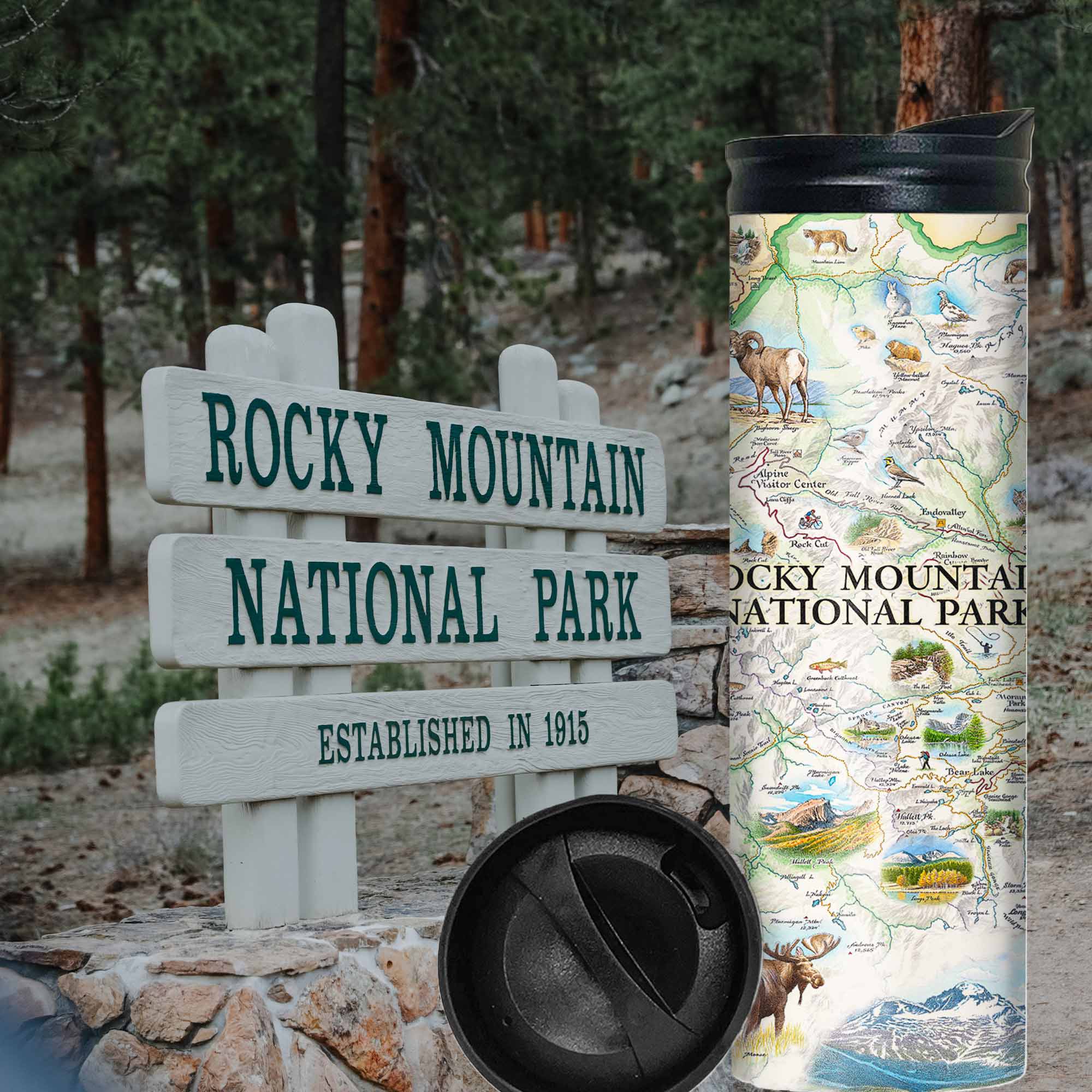 Rocky Mountain National Park Map 16 oz Travel Bottle. In the background is the Rocky Mountain National Park Sign with pine trees by it. The map features illustrations of places like Trail Ridge Road, Mount Ganby, Estes Park, and the Alpine Visitor Center. Flora and fauna include bobcats, snowshoe hares, Indian paintbrushes, and wild roses.
