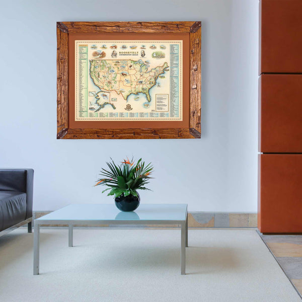 Roosevelt's USA Conservation Legacy hand-drawn hanging in an office above a table with a plant. The map print is framed in Montana hand-scraped pine with a brown mat.