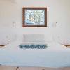 The San Juan Islands hand-drawn map hanging on a white wall over a bed with a white comforter and a blue throw blanket.