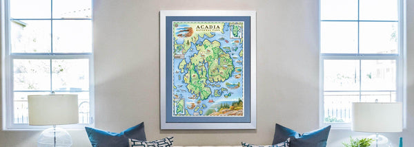 Acadia National Park hand-drawn map with a white frame and blue mat hangs above a couch with blue pillows.  