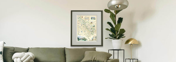 Banff National Park hand-drawn map in a wood frame. The print is hung above a sage green couch in a living room. 