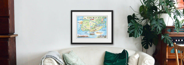 New Jersey's Cape May hand-drawn map in a black frame hanging on a wall in a family room near plants. 