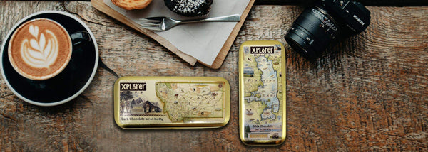 Map of Montana and Flathead Lake on a Chocolate Morsel Tin in dark and milk chocolate. The reusable tin is sitting on a table with coffee and a camera. 