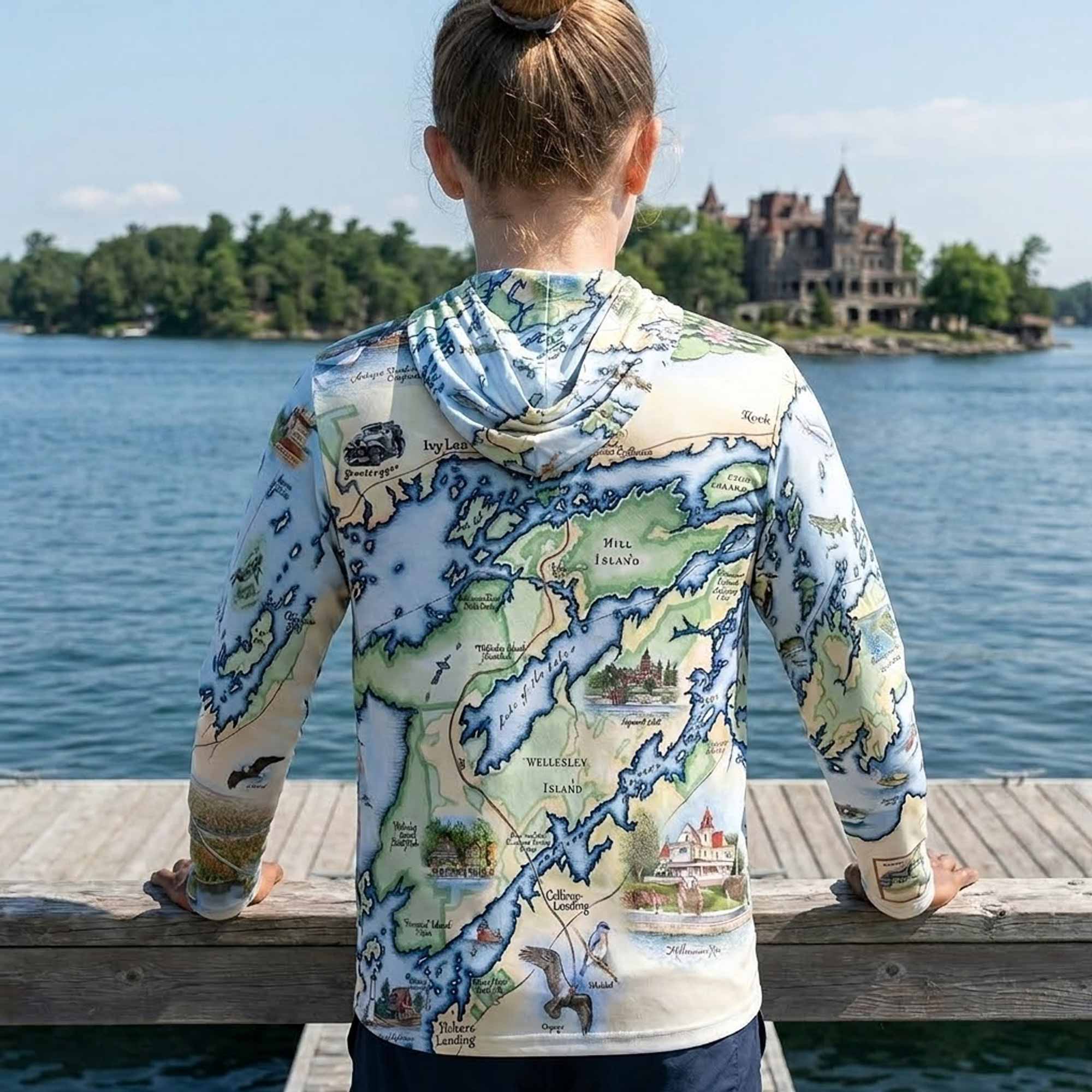 Person wearing a map-themed hoodie by a lake with a large building in the background