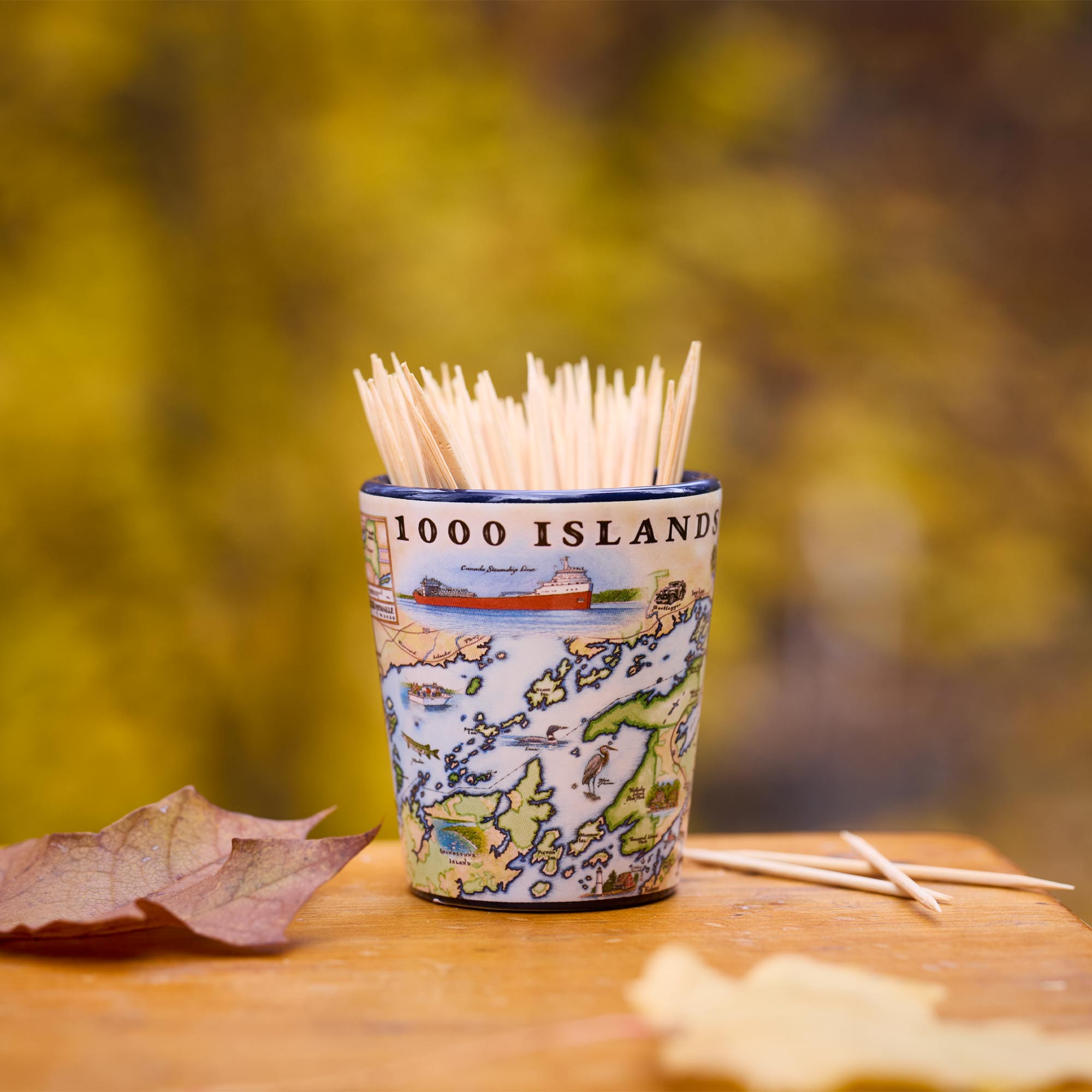 Shot glass with toothpicks labeled '1000 Islands' on a wooden surface with blurred natural background