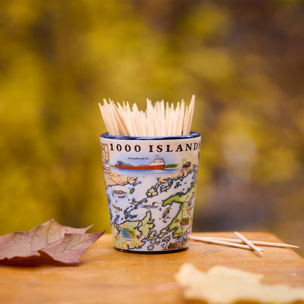 Shot glass with toothpicks labeled '1000 Islands' on a wooden surface with blurred natural background