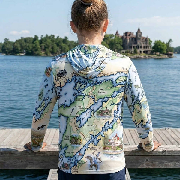 Person wearing a map-themed hoodie by a lake with a large building in the background