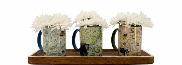 Three Coffee Mugs (Glacier, Flathead, Montana) sitting on a wooden tray. The mugs have white flowers in them. 