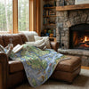 Person reading a book on a couch with a Acadia National Park map blanket in front of a stone fireplace.
