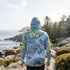 Person wearing a sun shirt hoodie with a map design of Acadia National Park standing on a rocky coastal path.