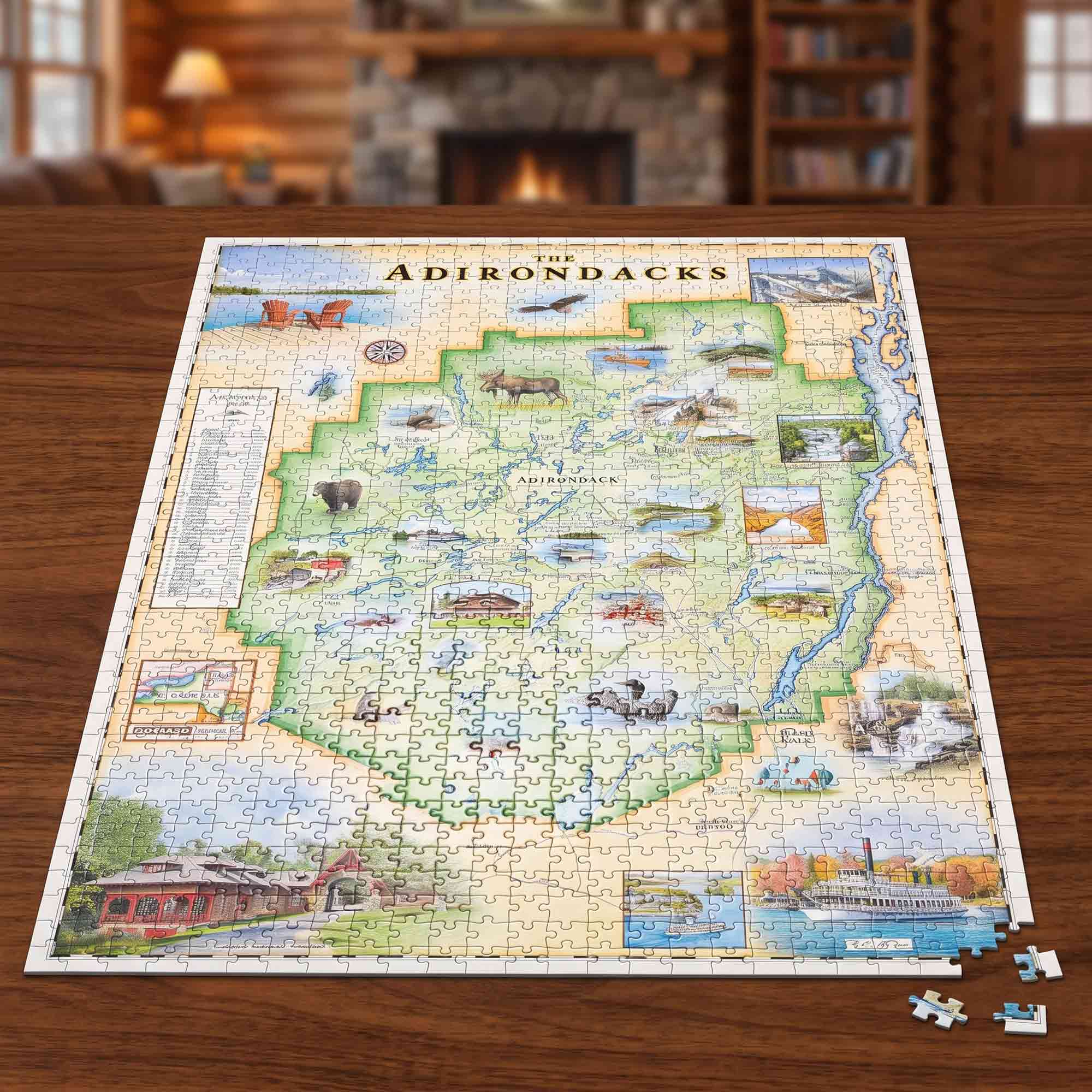 A completed jigsaw puzzle of The Adirondacks map spread on a wooden table, with a few loose pieces nearby and a blurred cozy indoor room in the background.