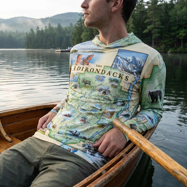 Person wearing a sun shirt hoodie with Adirondacks design, sitting in a boat on a lake.