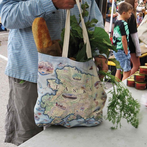 A man shopping at a farmers market with an Alaska Map Tote Bags by Xplorer Maps. The tote bag is filled with bread and vegetables.