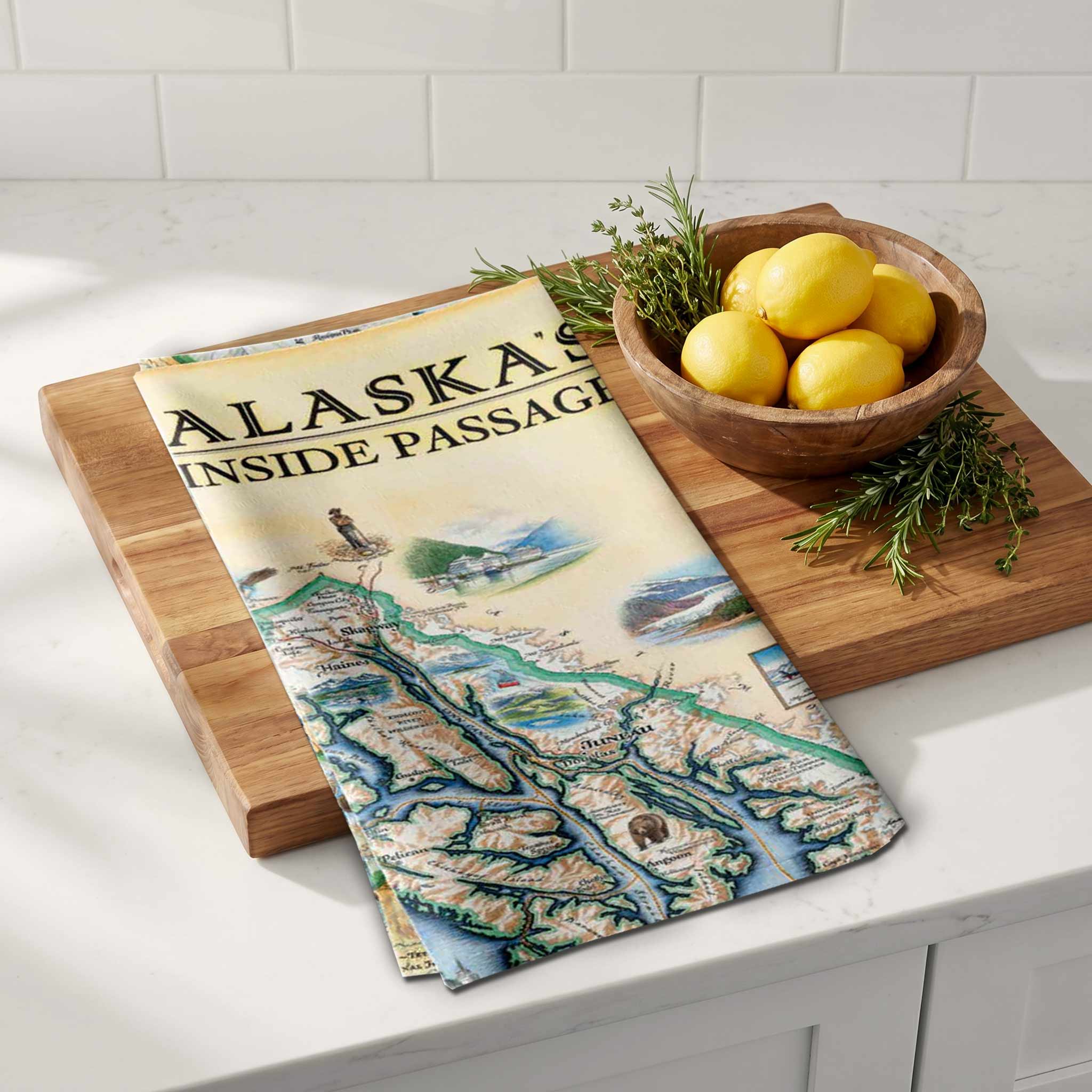 Wooden cutting board with a decorative towel featuring Alaska's Inside Passage design, placed on a kitchen counter.