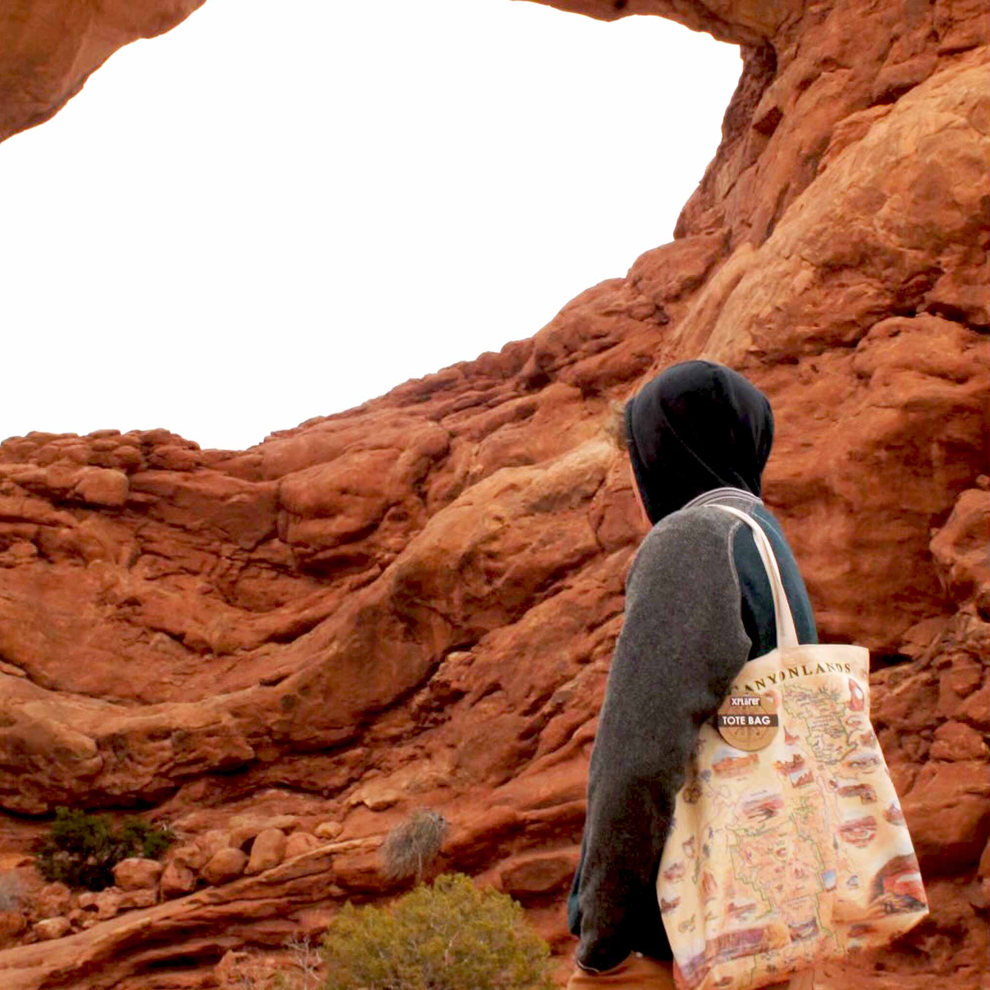 A man standing in front of the Arch in Arches and Canyonland National Parks carrying a tote bag by Xplorer Maps. 