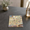 A rectangular printed coaster or tile featuring a detailed illustrated map and landscape scenes labeled 'Arches & Canyonlands,' placed on a dark stone tabletop with a small plant and glass bottle nearby.