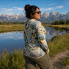 Woman in a scenic landscape with mountains and a lake, wearing a map-patterned sunshirt.