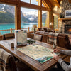 A person sits at a rustic wooden table in a cozy mountain lodge, assembling a detailed jigsaw puzzle of a map. The puzzle box, featuring the brand 'B&SEFE', stands nearby on the table, with a large window behind showing a stunning turquoise lake and snow-capped mountains.