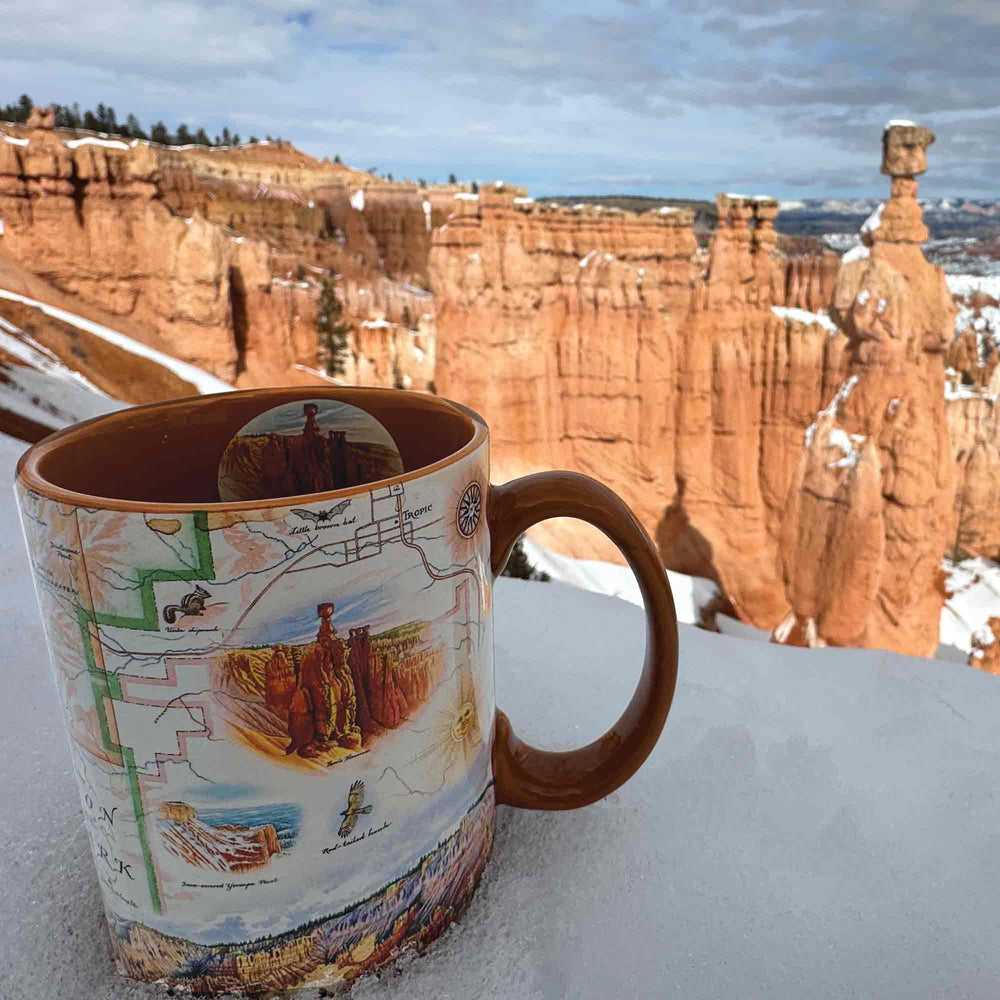 Orange 16 oz Bryce Canyon National Park Map Ceramic Mug amidst snow, showcasing canyons, hoodoos, horseback, Rim Trail, Sunrise Point, Sunset Point, Inspiration Point, Bryce Point.