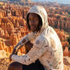 Person wearing a sun shirt hoodie with a Bryce Canyon map design, sitting against a backdrop of a canyon landscape.
