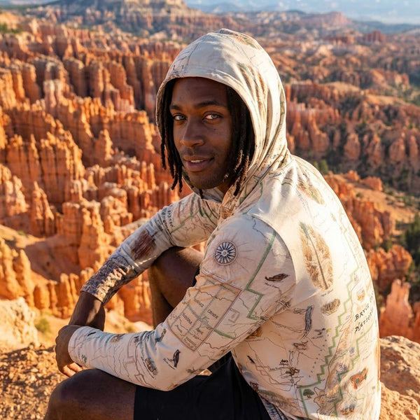 Person wearing a sun shirt hoodie with a Bryce Canyon map design, sitting against a backdrop of a canyon landscape.